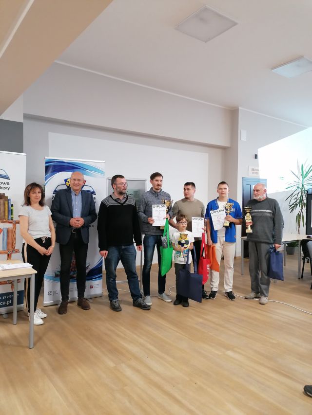 laureaci turnieju stoją z dyplomami i złotymi pucharami, w tle biała ściana