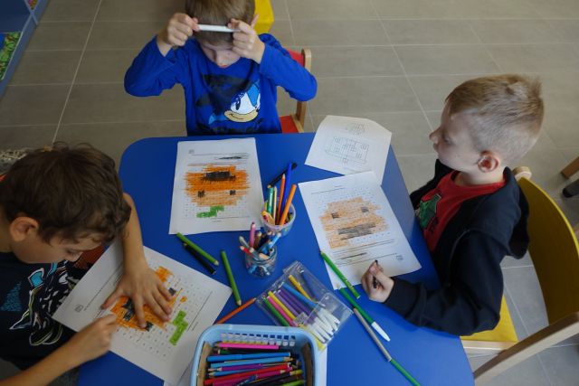 chłopcy siedzą przy niebieskim stoliku i wypełniają krzyżówki na kartkach