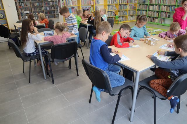 dzieci siedzą przy stolikach i malują na kartkach