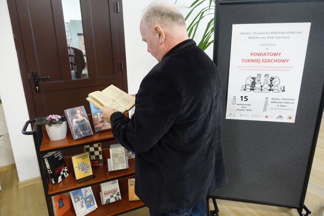 mężczyzna stoi przed wystawką książek o szachach