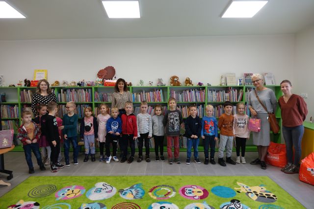 dzieci i 4 osoby dorosłe soją przed zielonymi regałami z książkami