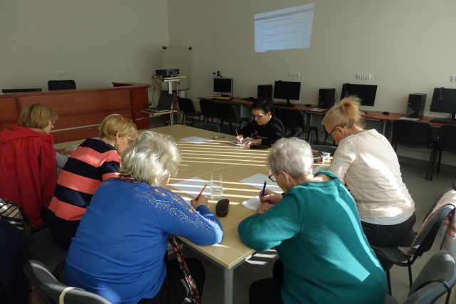 kobiety siedzą przy stołach połączonych i rozwiązują krzyżówki