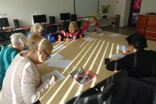 kobiety siedzą przy brązowych stołach i rozwiązują krzyżówki