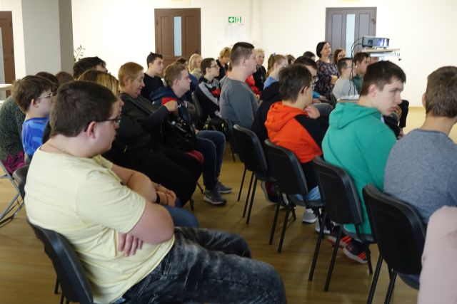 młodzież i opiekunowie siedzą na siwych krzesłach