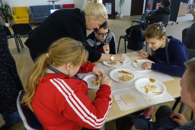 młodzież siedzi przy stole i robi z wafelków i ciastek kota