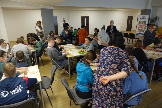 młodzież siedzi przy stolikach, na których mają papierowe talerzykii wykonują z wafekól, paluszków i biszkoptów koty