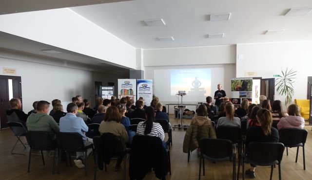 młodzież siedzi tyłem na krzesłąch, przed nimi biały ekran