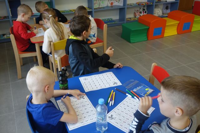 dzieci siedzą przy stolikach i wypełniają krzyżówki