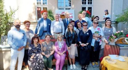 kobiety i mężczyźni siedzą i stoją, za nimi budynek muzeum