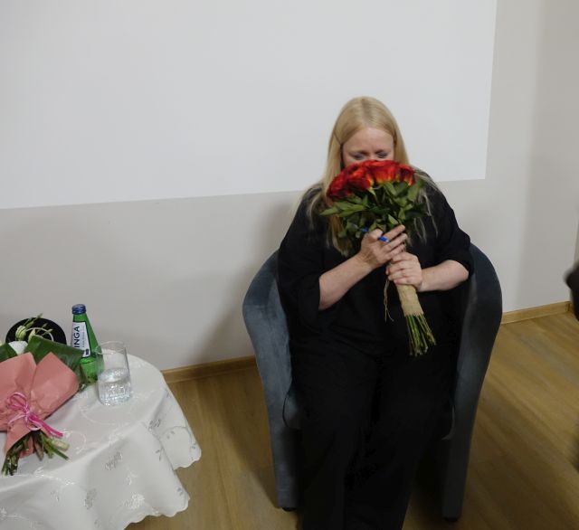 kobieta w czarnym kombinezonie z bukietem czerwonych róż