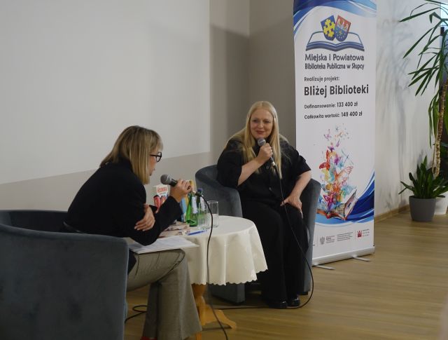 kobieta w czarnym kombinezonie i kobieta w czarnej bluzce siedzą przy stoliku