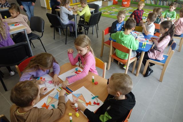 dzieci siedzą przy stolikach i rysują na kartkach