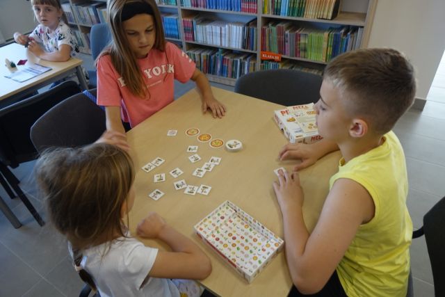 przy brązowym stole siedzą dzieci, na stole leżą gry planszowe