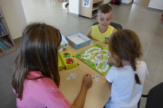 przy brązowym stole siedzą dzieci, na stole leżą gry planszowe