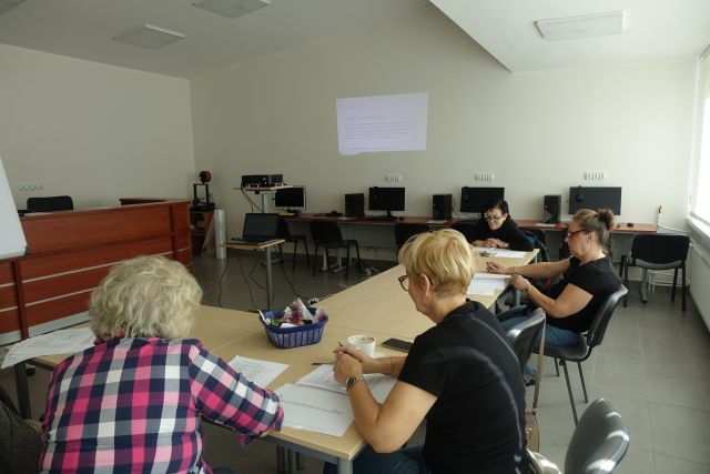 kobiety siedzą przy stołach , przed nimi kartki