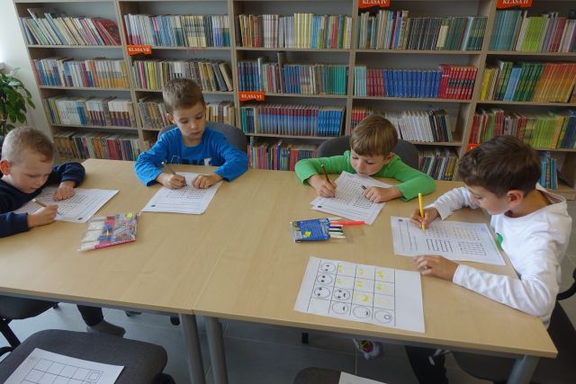 chłopcy siedzą przy stołąch i wykonują zadanie na kartkach