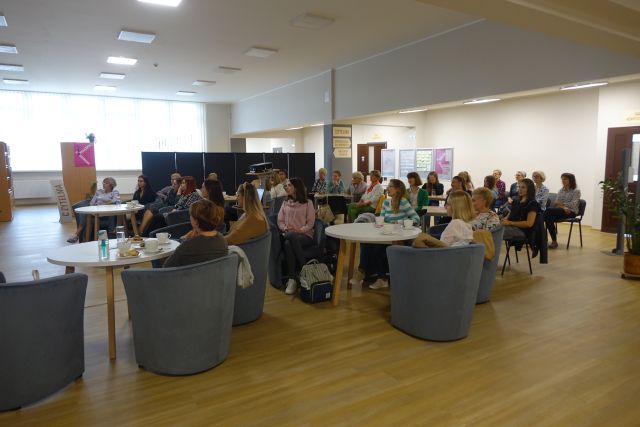 przy stolikach na siwych fotelach siedzą kobiety