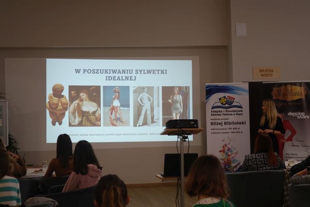 kobiety siedzą przy stlikach na siwych fotelach, przed nimi na białym ekranie ściennym na prezentacji 4 kobiety