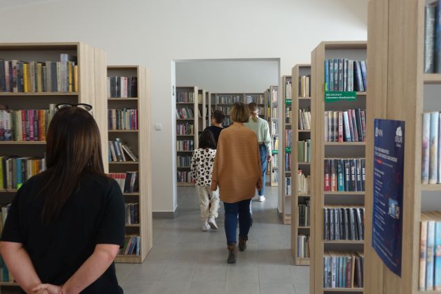 kobieta w brązowym swetrze i dzieci idą pomiędzy regałami z książkami