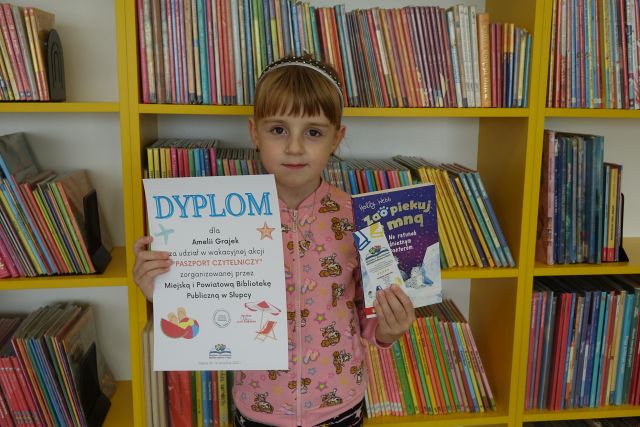 dziewczynka w różowej bluzce trzyma dyplom i książkę