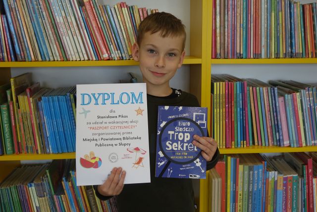 chłopiec w czarnej bluzce trzyma dyplom i książkę