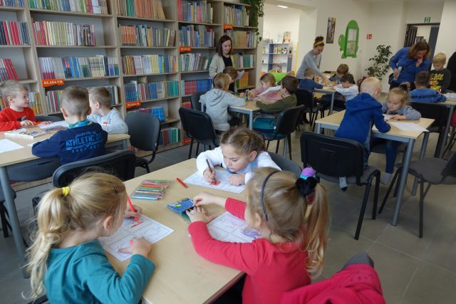 dzieci siedzą przy stolikach i malują potworki