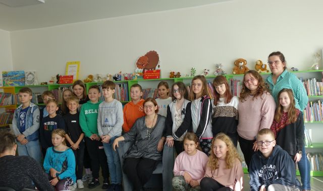 dzieci uczestniczące w spotkaniu pozują do zdjęcia z autorką, w tle regały z książkami