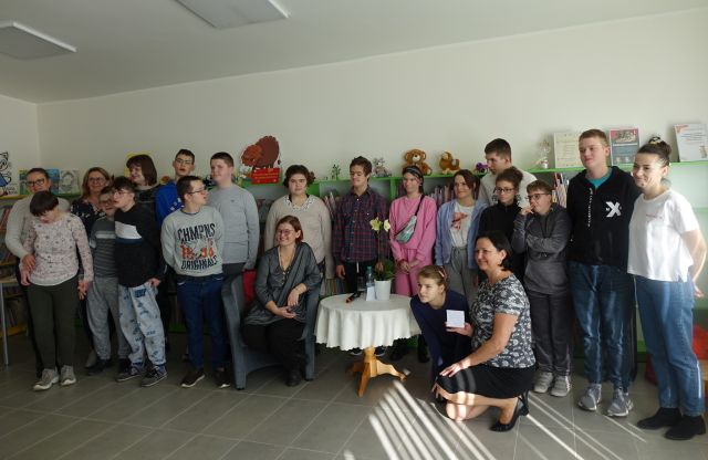 dzieci uczestniczące w spotkaniu pozują do zdjęcia z autorką, w tle regały z książkami