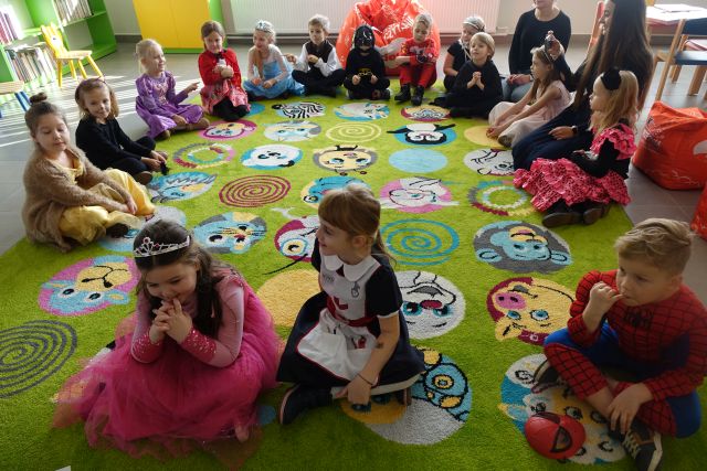 na zielonym dywanie siedzą dzieci w stroch postaci z bajek