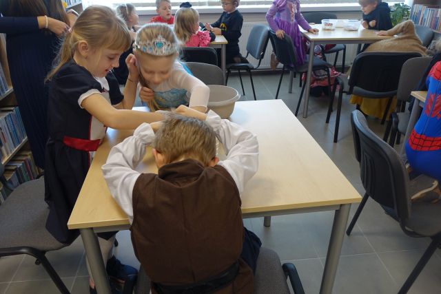 dzieci w strojach postaci z bajek siedzą przy stołach i przekładają fosolki do pojemników