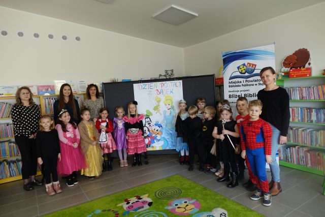 dzieci w strojach postaci z bajek stoją na tle regałów z książkami