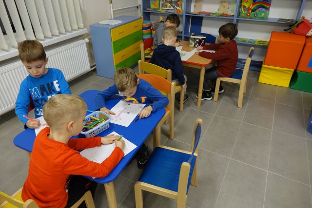 przy niebieskim i brązowym stoliku siedzą chłopcy i rozwiązują zadania