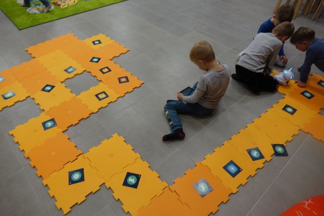 na podłodze rozłożone duże żółte puzle, przed nimi siedzi chłopiec z tabletem