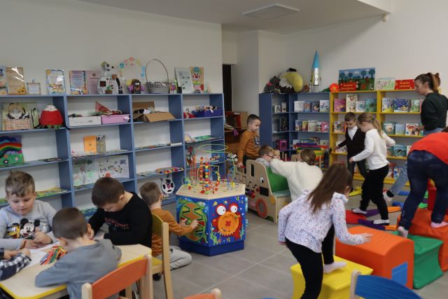 dzieci bawią się przy zabawkach sensorycznych, w tle niebieskie regały biblioteczne