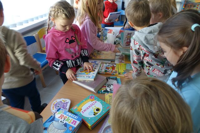 dzieci stoją przed stołami i oglądają książki