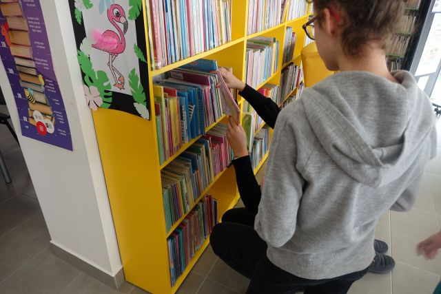 młodzież szuka książek na żółtym regale