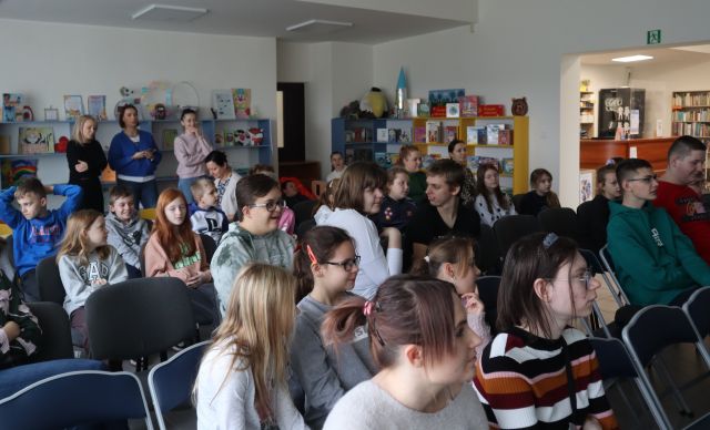 uczestnicy spotkania siedzą na krzesłach, w tle pomieszczenie biblioteczne