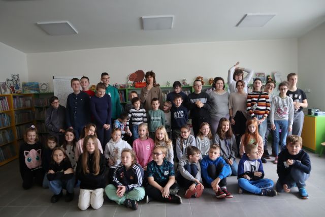 uczestnicy spotkania pozują do zdjęcia z autorem, w tle regały z ksiżkami