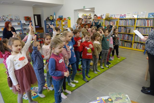 dzieci stoją na zielonym dywanie, w tle regały z książkami