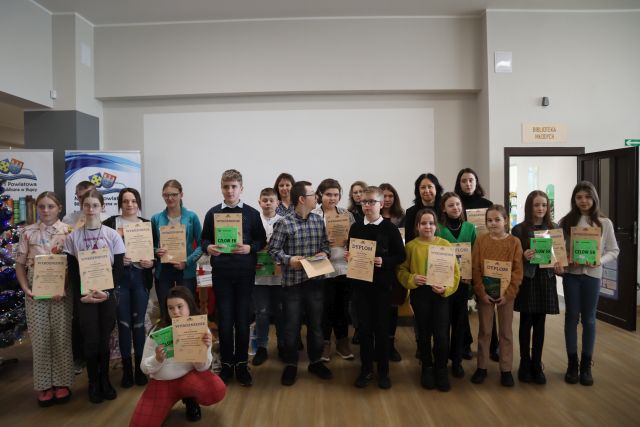 w trzech rzędach stoją osoby nagrodzone w konkursie, z lewej strony ubrana choinka