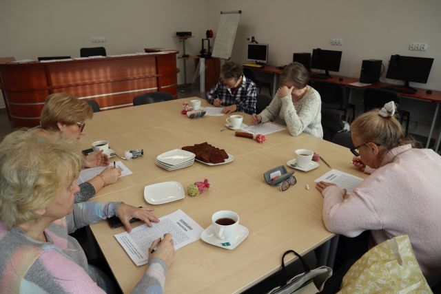 5 kobiet siedzi przy stołach i rozwiązuje krzyżówki