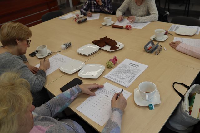 5 kobiet siedzi przy stołach i rozwiązuje krzyżówki