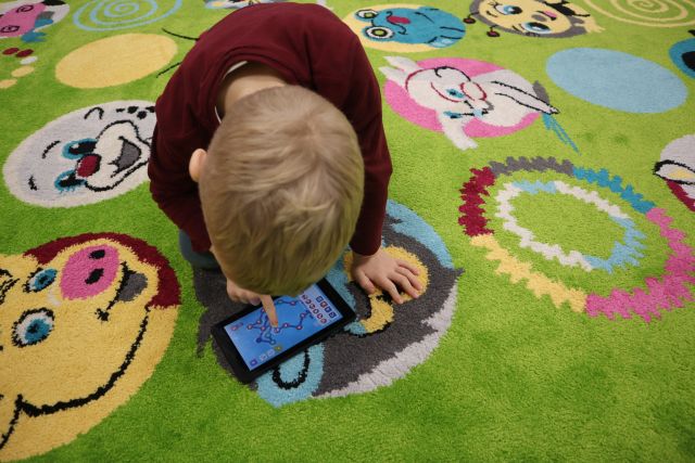 chłopiec klęczy na ziemonym dywanie i steruje robotem na tablecie