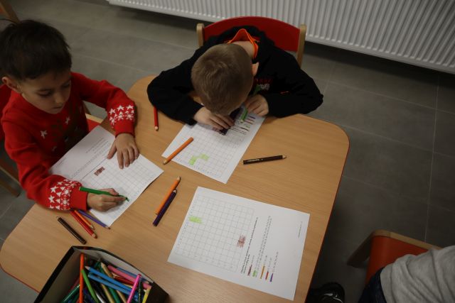 dzieci siedzą przy stole brązowym i rozwiązują krzyżówki