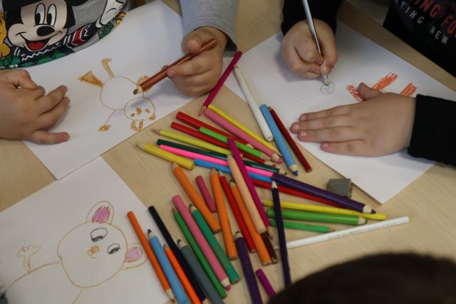 na stole leżą kartki i kredki, dzieci malują