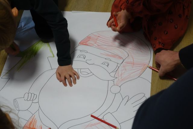 dzieci zamalowują zarys mikołaja na dużej kartce