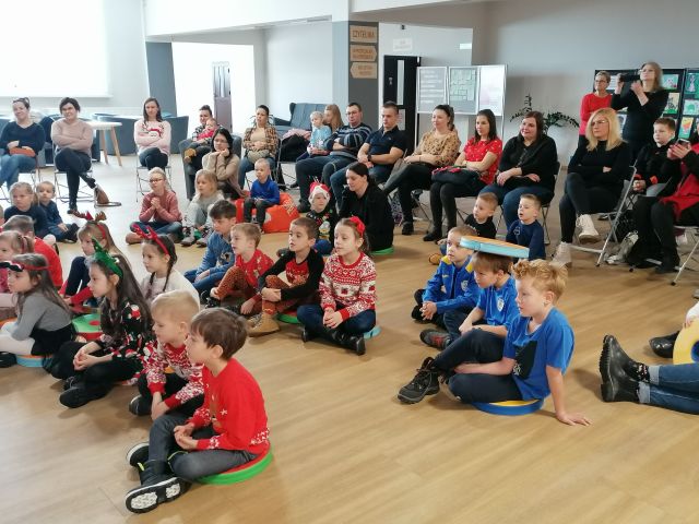 dzieci siedzą na podłodze, a rodzice za nimi na krzesłach