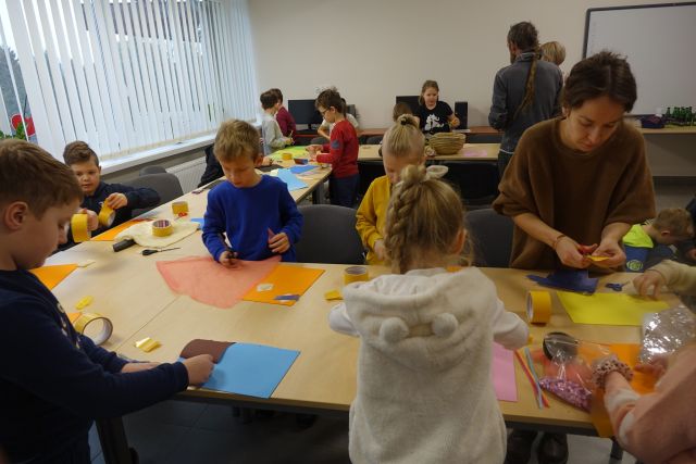 dzieci siedzą przy brązowych stołach i naklejają materiały na kartki