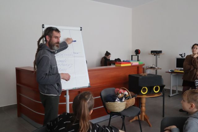 mężczyzna w siwej bluzie pisze na flipcharcie, w tle brązowe biurko