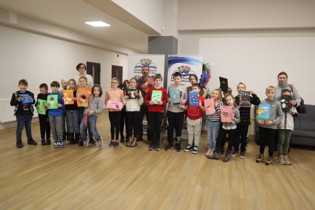 dzieci - uczestnicy warsztatów stoją i w rekach trzymają wykonane przez siebie prace